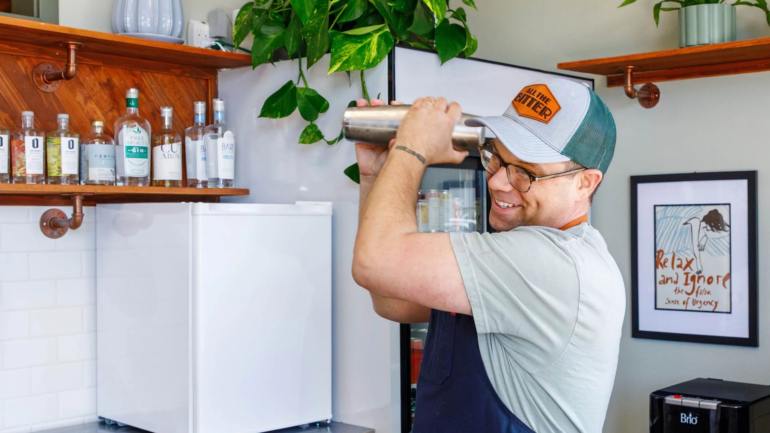 Person holding a cocktail shaker in a bar setting with bottles and decor in the background