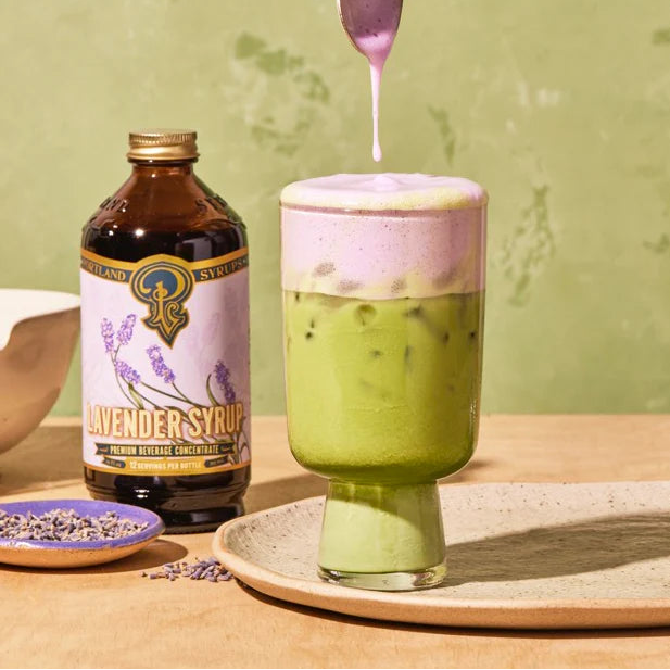 Dropping lavender foam on an iced matcha drink with a bottle of Portland Syrups Lavender Syrup.