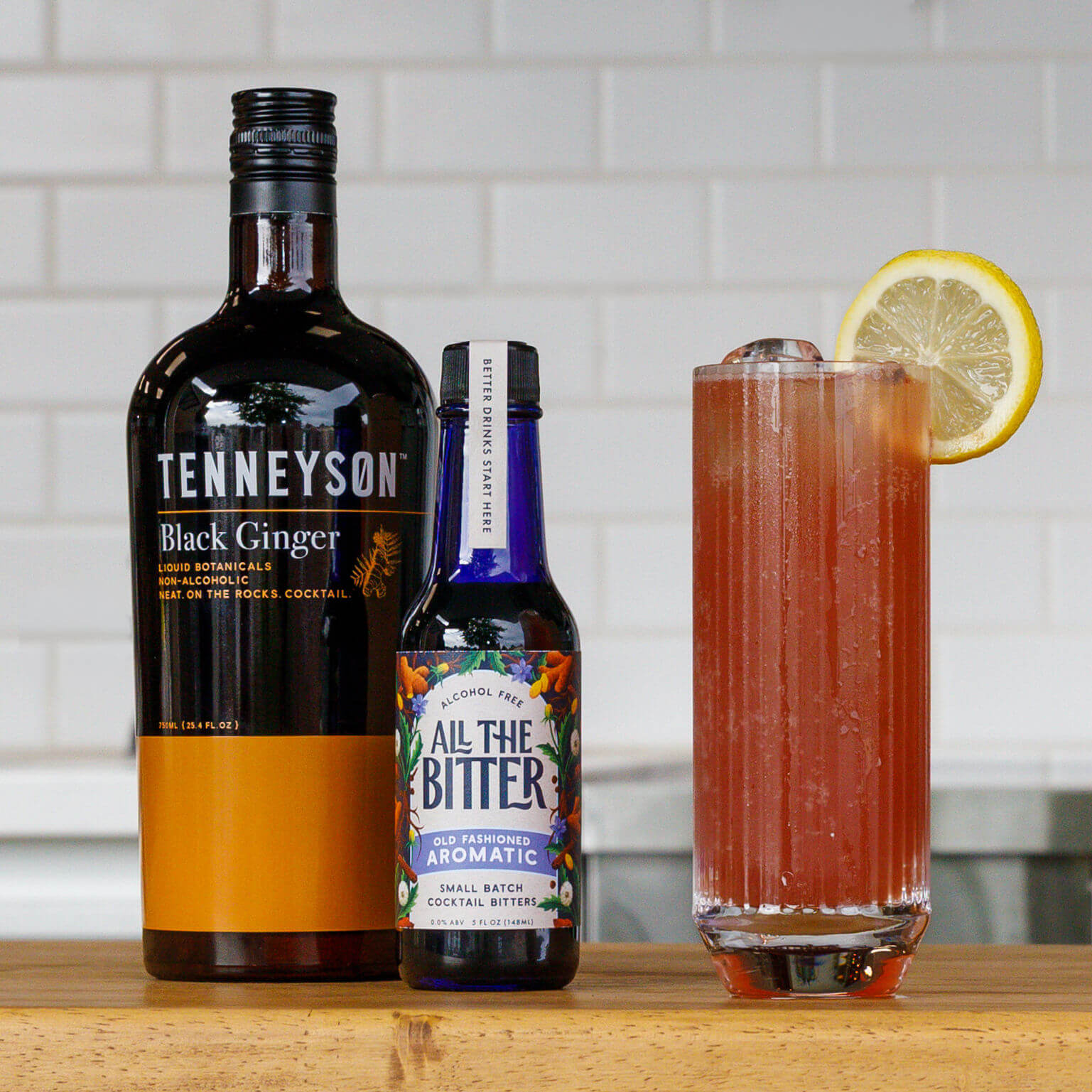 Bottle of Tenneyson Black Ginger and All the Bitter with a non-alcoholic cocktail on a wooden surface.
